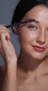 Zarif güzellik sahnesi profesyonel fırçayla kaş tarama rutinini gösteriyor. Yumuşak sinematik ışıklandırma doğal zarafeti yakalar. Cilt bakımı reklamları ve sosyal medya içeriği için mükemmel.
