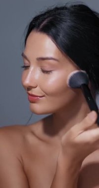 Serene güzellik portresi zarif fırça uygulaması ile kadınların makyaj rutinini yakalıyor. Gri üzerine yumuşak doğal estetik. Sağlık kampanyaları ve yaşam tarzı güzellik içeriği için ideal..