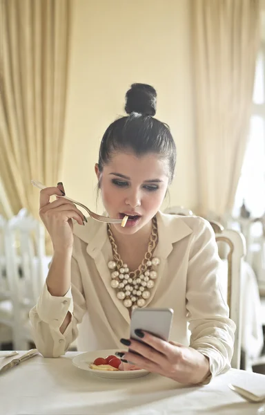 Kobieta jedzenie i sprawdzanie telefonu — Zdjęcie stockowe