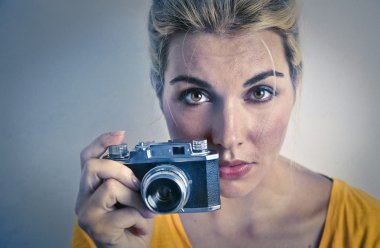 Genç sarışın kız eski bir kamera ile sağ elini tutuyor ve kendine güvenen görünüyor