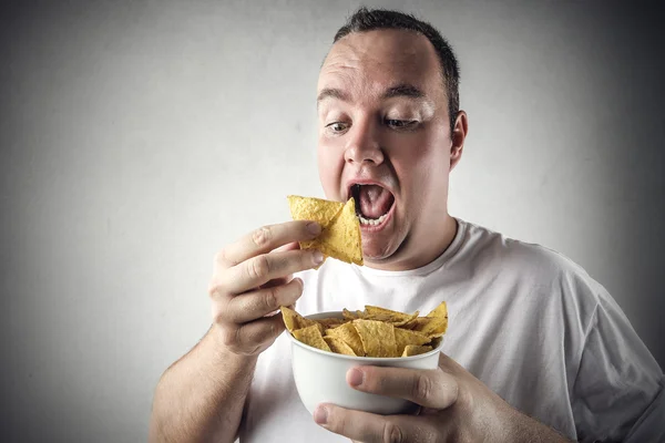 Obtloustlý muž jíst chipsy z mísy — Stock fotografie