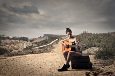 Girl playing guitar on a dusty road