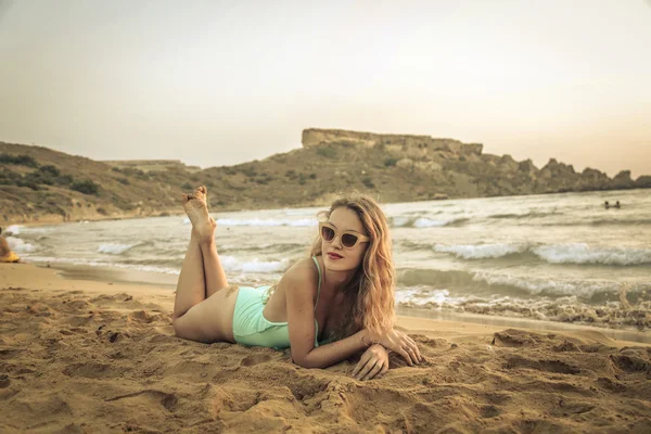 Prachtige blond meisje liggend in het zand bij zonsondergang — Stockfoto