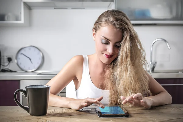 Blond flicka sitter på en köksbänk med en tablett — Stockfoto