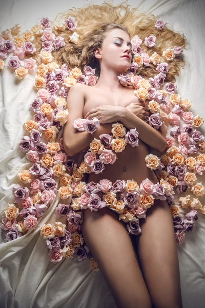 Молодая красивая блондинка спит в кровати, покрытой розами — стоковое фото