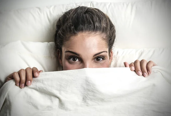 Beautiful girl hiding herself behind the sheets — Stock Photo, Image