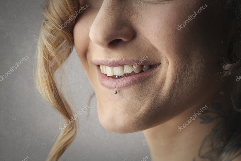 Detalhe de um piercing labret na boca de uma mulher sorridente