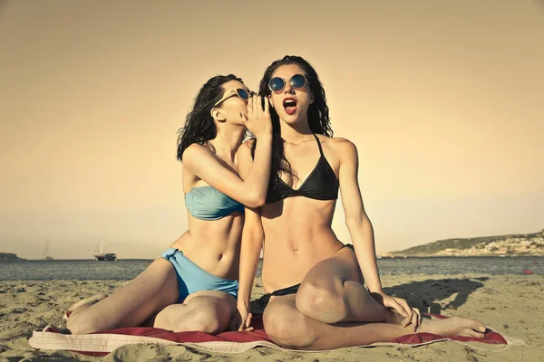 Dos amigos en la playa susurrando secretos — Foto de Stock