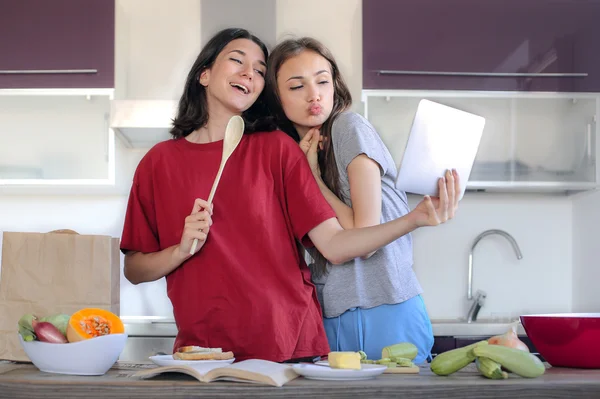 Two young women standing in the kitchen cooking some food — Stock Photo, Image