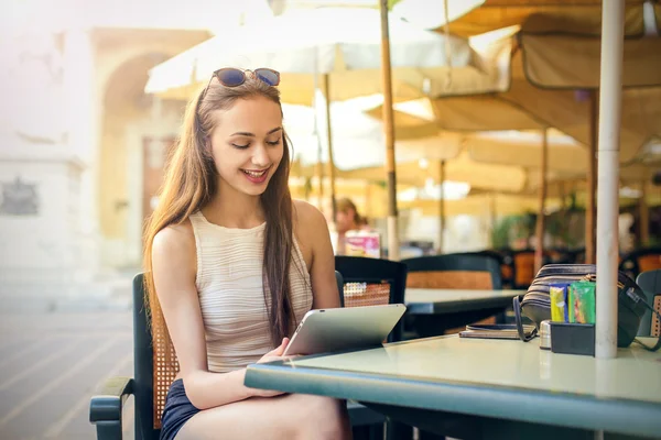 Menina bonita lendo algo em um tablet em um café — Fotografia de Stock