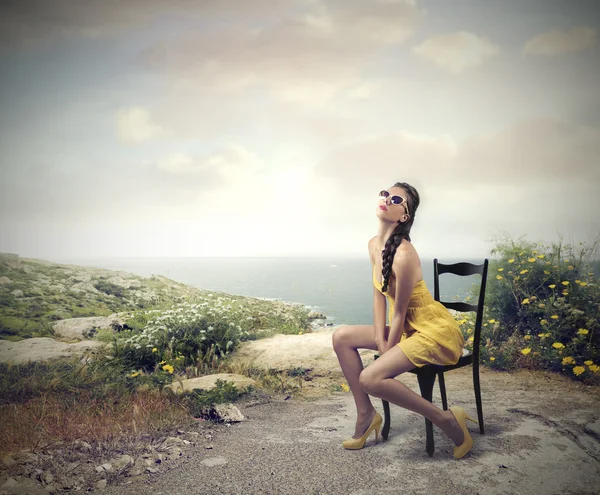 Όμορφη γυναίκα που κάθεται σε μια καρέκλα μπροστά στη θάλασσα — Φωτογραφία Αρχείου