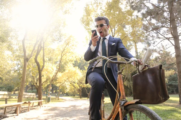 Geschäftsmann im Park, der sein Smartphone beim Fahrradfahren benutzt — Stockfoto