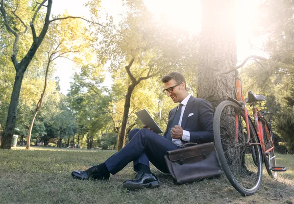 Бизнесмен, сидящий в парке, используя технологии — стоковое фото