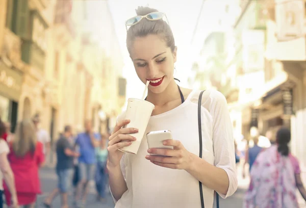 Ung flicka kontrollera sin telefon när man dricker en milkshake — Stockfoto