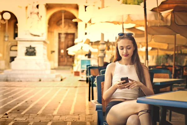 Mladá žena pomocí svého telefonu při posezení v kavárně — Stock fotografie