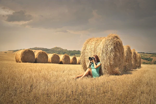 Menina sentada em um campo de grãos tirando uma foto — Fotografia de Stock