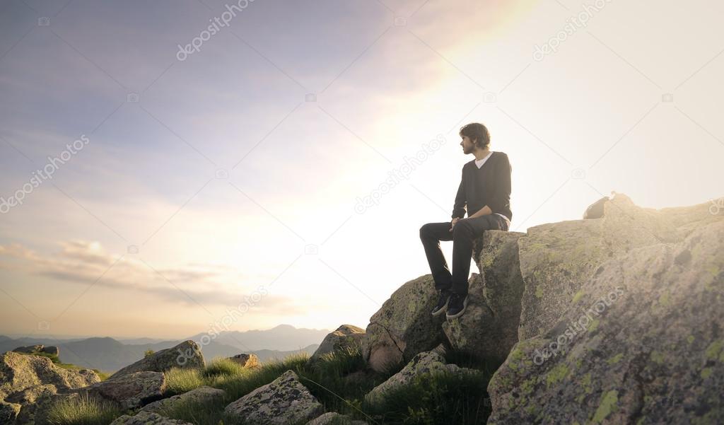 Man sitting on a rock looking far away