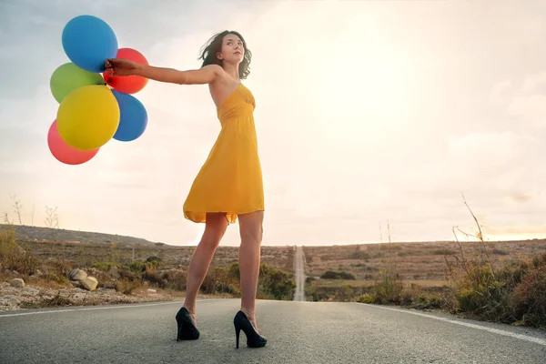 Flickan bär en gul klänning, med färgglada ballonger — Stockfoto