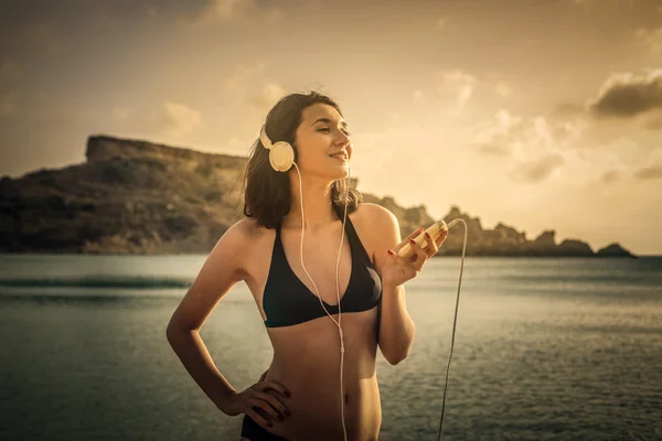 Jovem mulher ouvindo música na praia — Fotografia de Stock