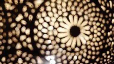 Aydınlatılmış, Fas yapımı, karmaşık çiçek desenli Arap pirinçten bir lambanın soyut yakın çekimi. Fas ve Arap lamba tasarımı kavramı. Görüntü bulanıklığından hareket eden soyut arkaplan görüntüsü, odak noktasına odaklanmış.