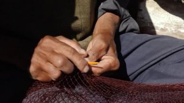 Yaşlı bir balıkçı, Essaouira, Fas 'taki limanda iğne ve iplikle ticari bir balık ağını onarıyor. El işi..