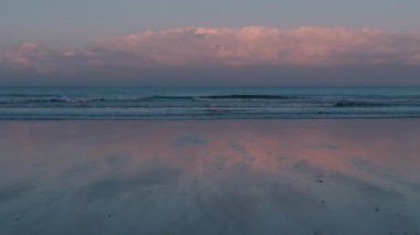 Huzurlu plaj sahnesi, gelen dalgalar, pembe yumuşak bulutlar ve şafakta yansımalar. Meditasyoncu, rahatlatıcı SPA konsepti, rahatlatıcı arka plan görüntüleri. Yavaş çekim.