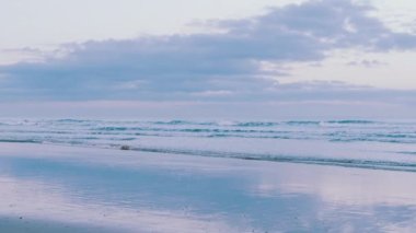 Tranquil beach scene with waves, clouds, and reflections, pink sky. Meditative, calming SPA concept, background footage. Slow-motion.