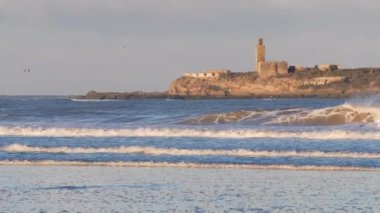 Fas 'taki Essaouira sahilinde camili, eski binalı, harabeli bir ada manzaralı açık deniz dalgaları. Turistik seyahat beldesi Fas.