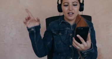 Genç çekici Faslı Arap kadın kulaklık takarak cep telefonundan müzik dinliyor. Gerçek zamanlı görüntüler.