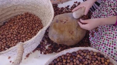 Faslı bir kadın geleneksel el yapımı Argan yağı üretimi için Argan cevizlerinin dış kabuğunu açıyor. Meşhur Argan yağı fındıkların içindeki çekirdeklerden elde edilir. Yağ yağ asitleri açısından zengindir ve yemek ve kozmetik ürünlerinde kullanılır..