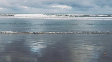 Bulutlu gökyüzü, yansımalar ve gelen dalgalarla sabah sahili manzarası. Doğanın arka plan görüntüleri. Yavaş çekim.