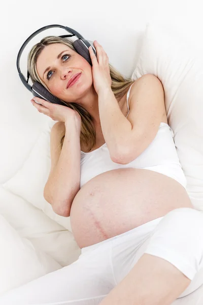 Pregnant woman with headphones resting in bed — Stock Photo, Image