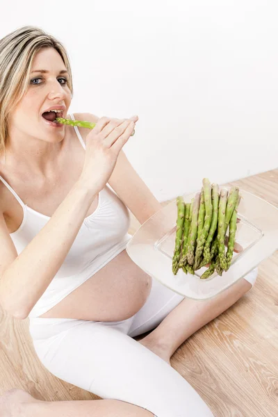 Mulher grávida comendo espargos verdes — Fotografia de Stock