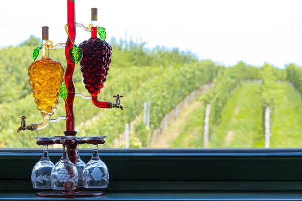 glass carafe with white and red wine in the shape of a grape and vineyard background