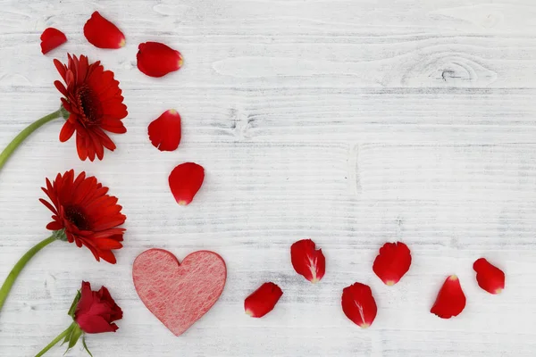 Beyaz ahşap arka planda kırmızı kalpli kırmızı çiçekler.