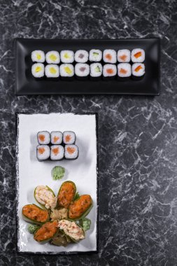 Siyah taşlı arka planda deniz mahsullü suşi ruloları.