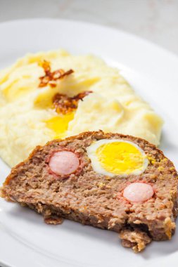 Yumurta dolu köfte ve patates püresi ve kızarmış soğanla servis edilen sosis.
