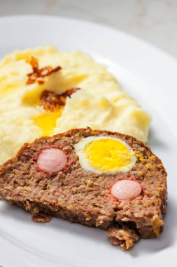 Yumurta dolu köfte ve patates püresi ve kızarmış soğanla servis edilen sosis.