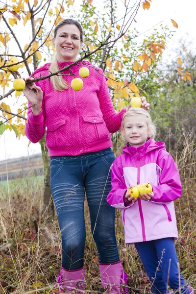 Mother and her daughter with autumnal apple tree holding an apples