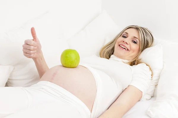 Gravid kvinna vila i sängen med ett grönt äpple — Stockfoto