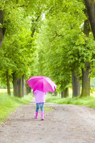 Malá dívka, která nosí gumové boty s deštníkem v jarní ulici — Stock fotografie
