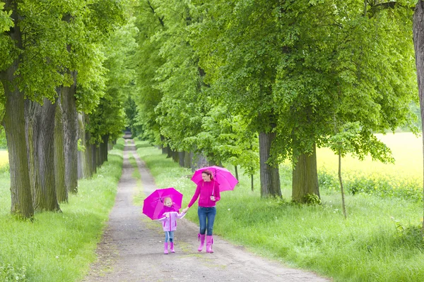 Mother and her daughter with umbrellas in spring alley — Stock Photo, Image