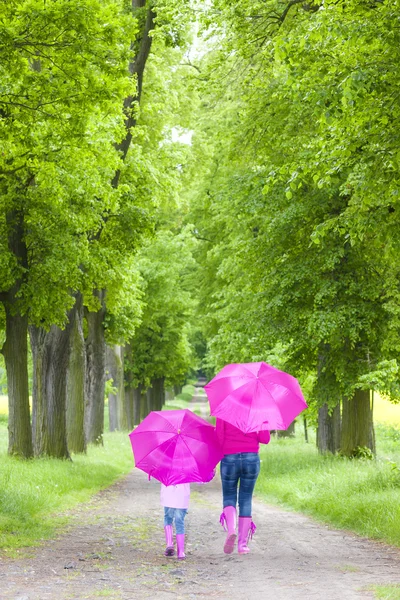 Mãe e sua filha com guarda-chuvas no beco da primavera — Fotografia de Stock