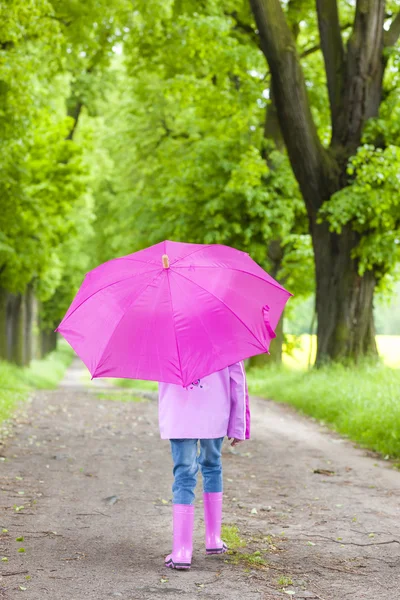 Little girl wearing rubber boots with umbrella in spring alley Stock Image