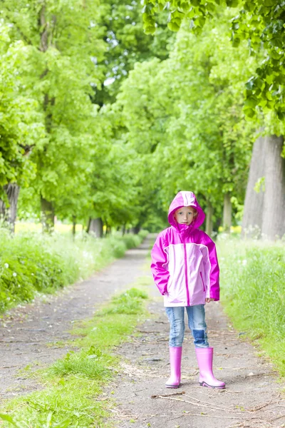 Liten flicka klädd i gummi stövlar i våren gränd — Stockfoto