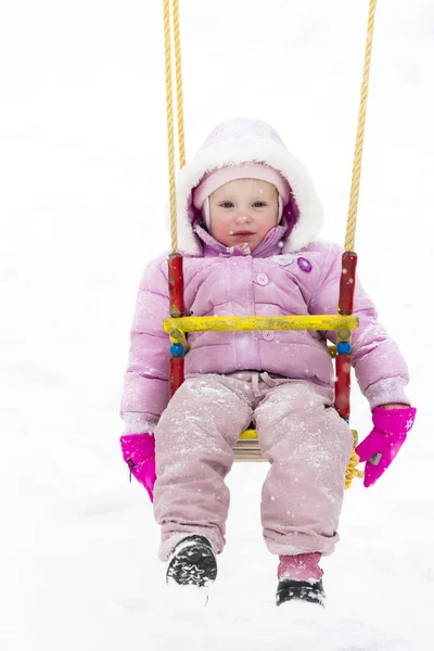 Liten flicka sitter på swing på vintern — Stockfoto