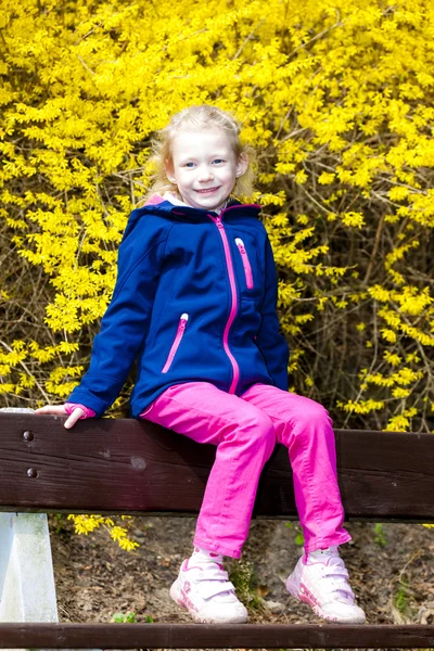 Kleines Mädchen sitzt im Frühling auf Bank — Stockfoto