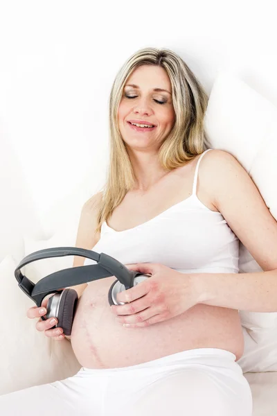 Pregnant woman with headphones resting in bed — Stock Photo, Image