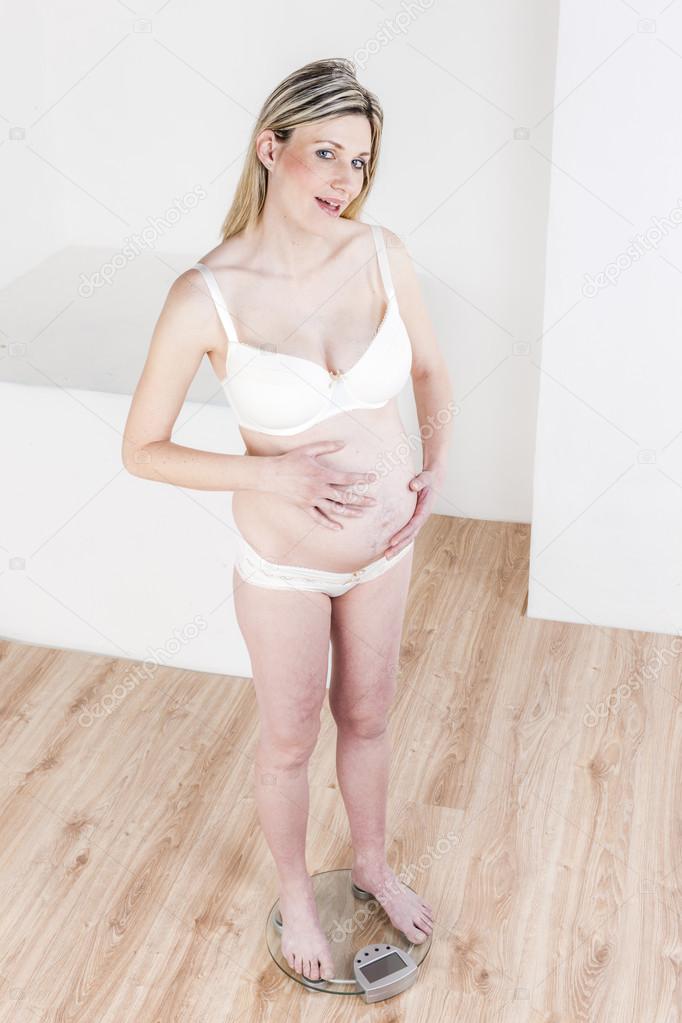 Pregnant woman wearing lingerie standing on a weight scale