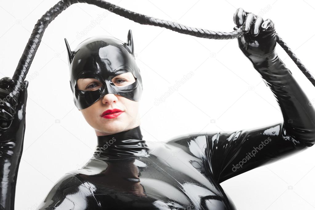 Standing woman wearing latex clothes with a whip